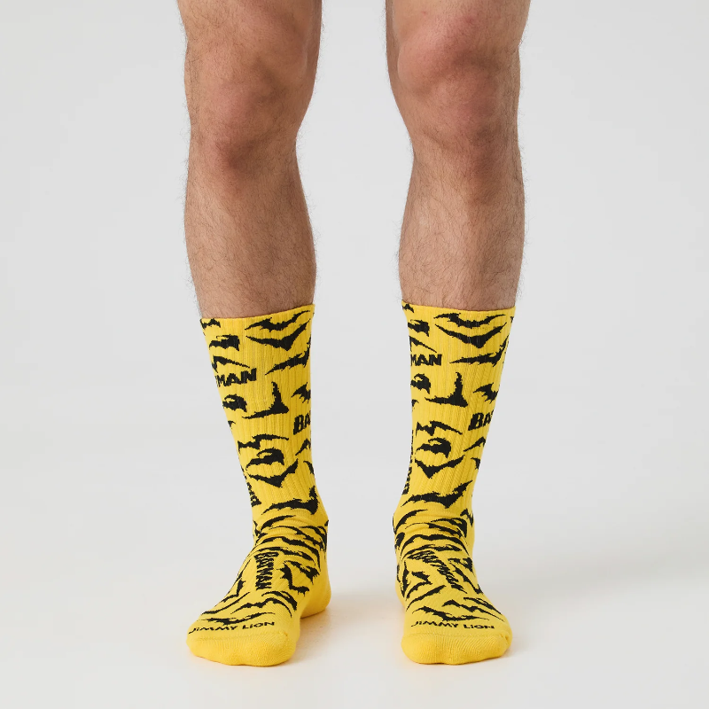 A person's legs wearing bright yellow crew socks with a black tiger-stripe pattern and black text, photographed against a clean light gray studio background.